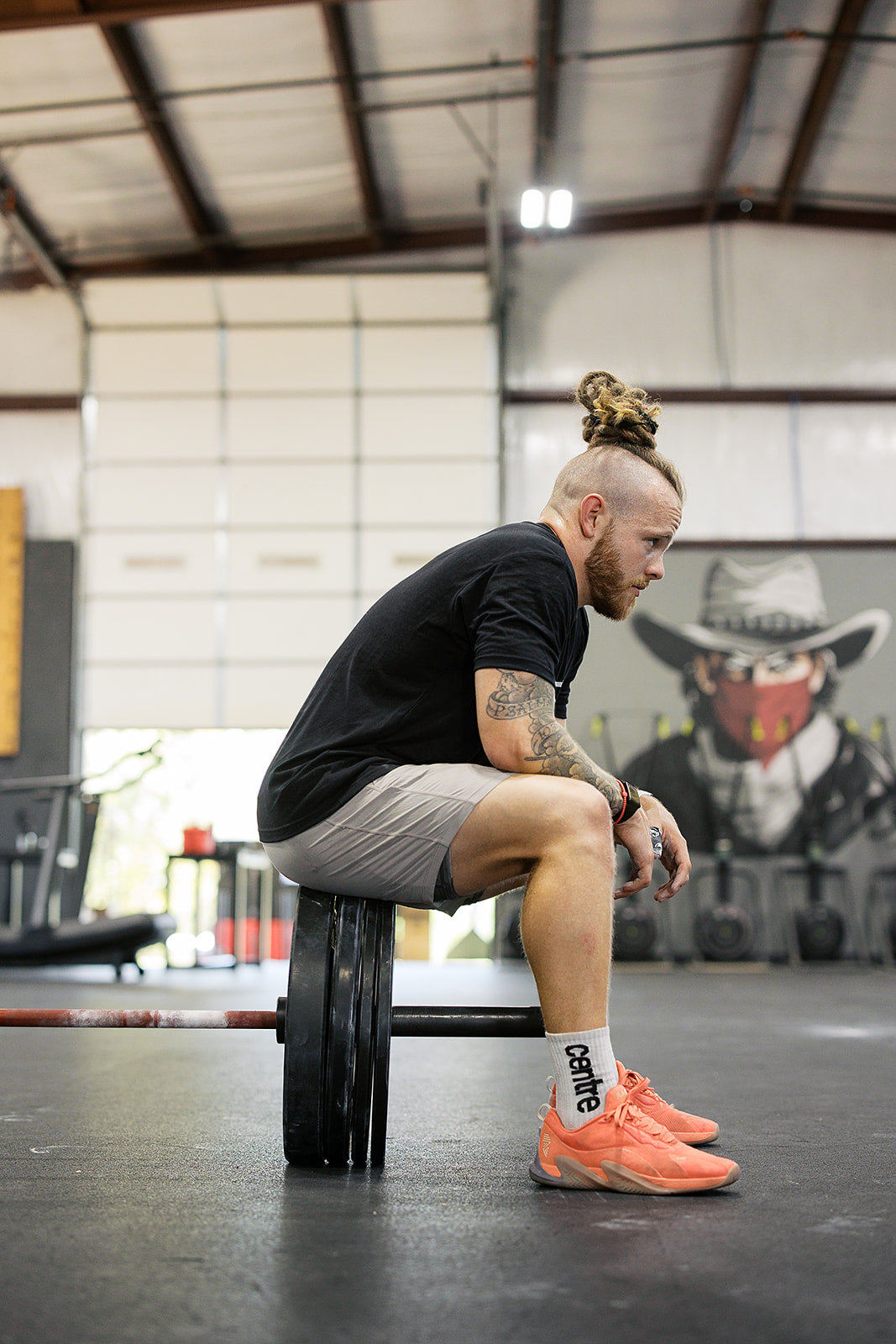 Athlete sitting on the plates of a loaded barbell, looking down at the gym floor in a moment of reflection.