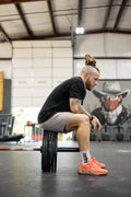 Athlete sitting on the plates of a loaded barbell, looking down at the gym floor in a moment of reflection.