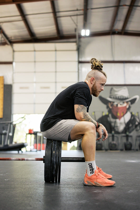 Athlete sitting on the plates of a loaded barbell, looking down at the gym floor in a moment of reflection.